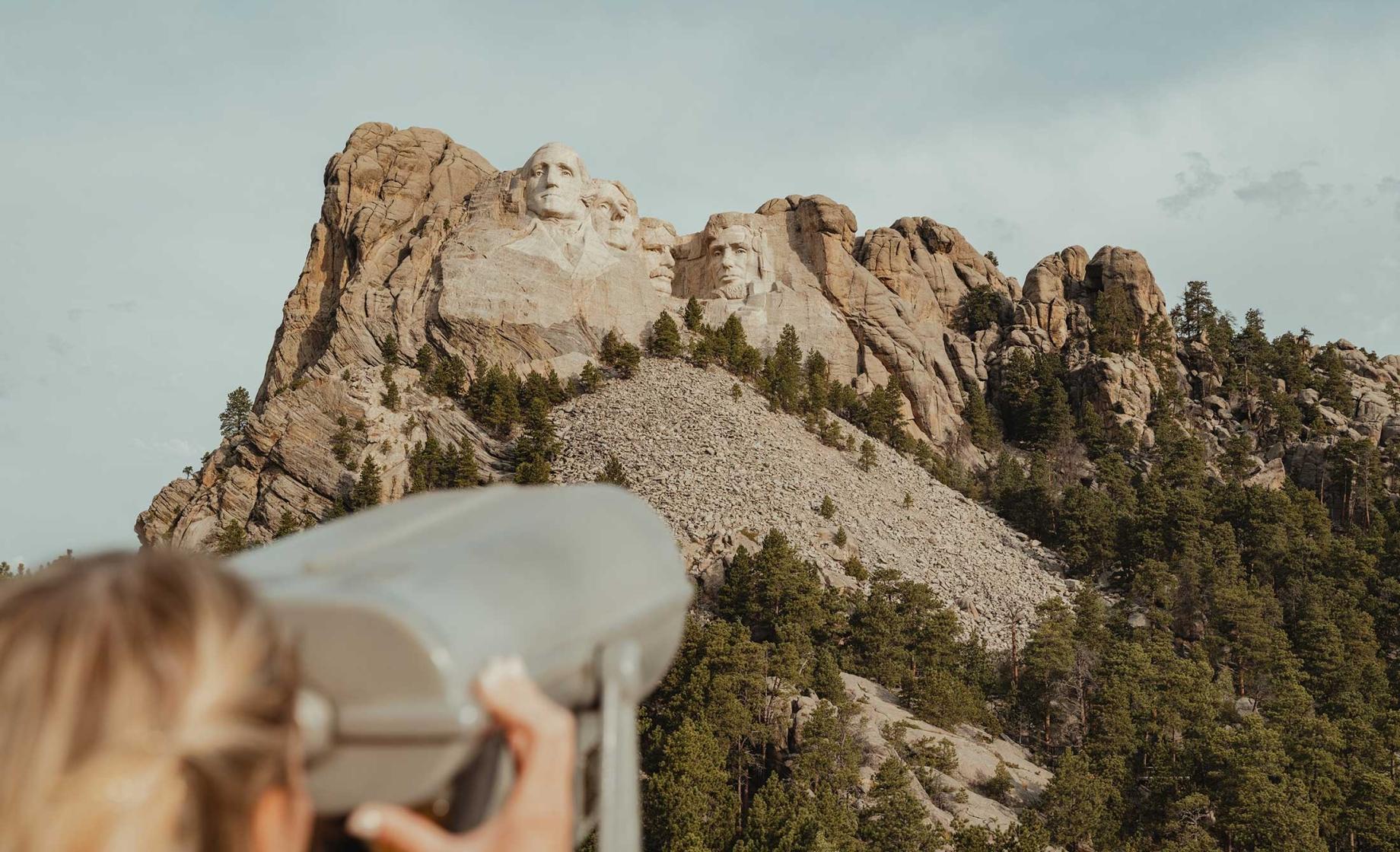 Woman using standing binoculars to view Mt. Rushmore in the distance